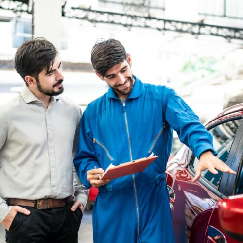 Vehicle maintenance handsome man servicer explain car condition, point at vehicle part to male customer in garage. Automotive mechanic hold automotive checklist document. Car repair service concept.
